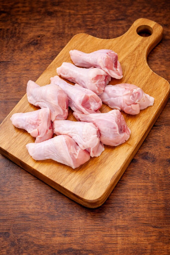 Alitas de pollo crudas sobre tabla de madera listas para marinar y cocinar en kamado