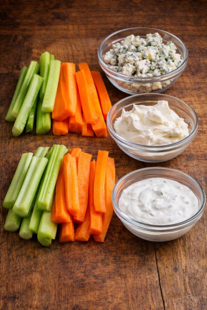 Bastones de apio y zanahoria acompañados de queso azul, queso crema y salsa ranch sobre mesa rústica