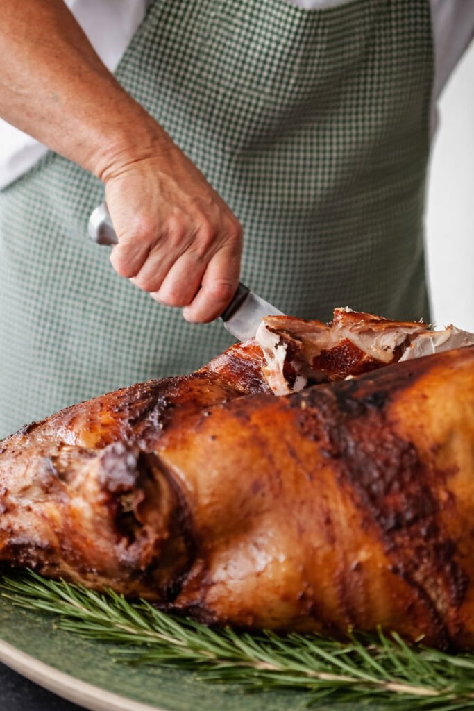Corte de lechón a las brasas en kamado con piel crujiente durante el asado