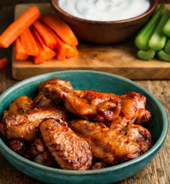 Buffalo wings en kamado glaseadas con salsa picante servidas en plato azul sobre mesa rústica