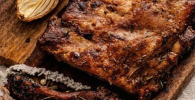 Costillas de cerdo en kamado doradas y jugosas sobre tabla de madera con hierbas aromáticas