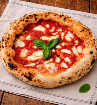 Pizza artesanal al kamado con tomate, mozzarella fundida y albahaca fresca sobre mantel rústico y mesa de roble